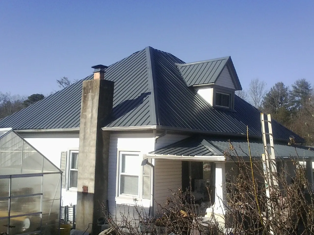 Dark blue standing seam metal roof on a white farmhouse with dormer — Slate & Tile Roof Repair by Roofing Brothers in Shallotte