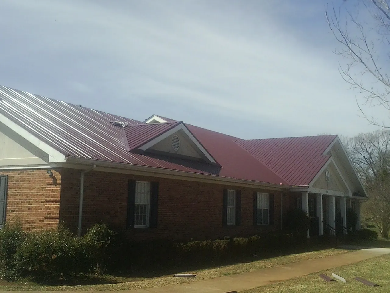 Red metal roof with gabled entries on a long brick building, from a Hail Damage Roof Repair job in Shallotte