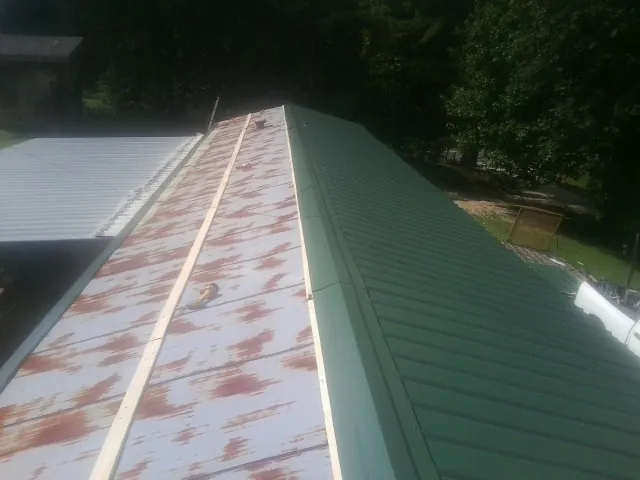 Old rusted panels beside newly installed green metal roofing — Wind Damage Roof Repair by Roofing Brothers in Shallotte