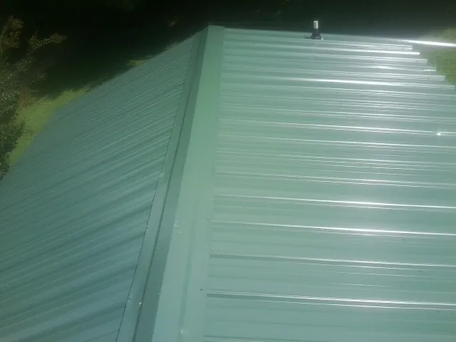 New green metal panels meeting at the ridge of a roof — Flat Roof Repair work by our crew in Shallotte