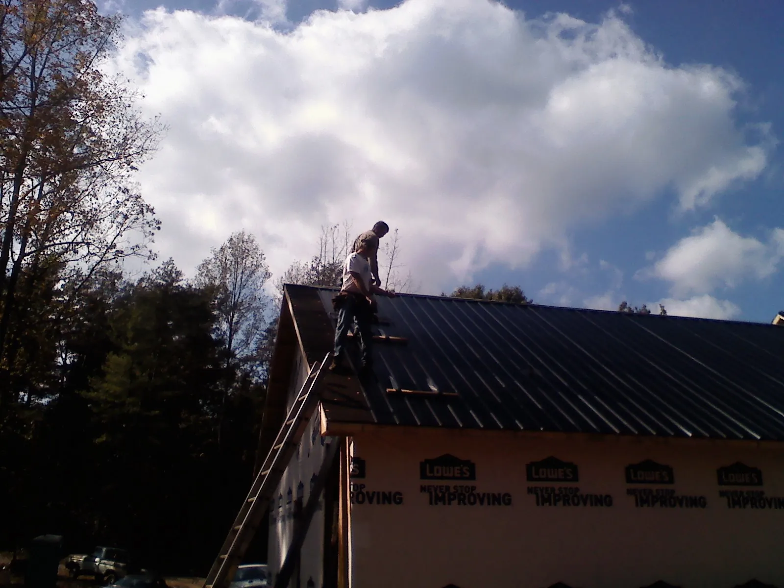 Roofer fastening dark metal panels high against a cloudy sky, from a Roof Inspection job in Shallotte